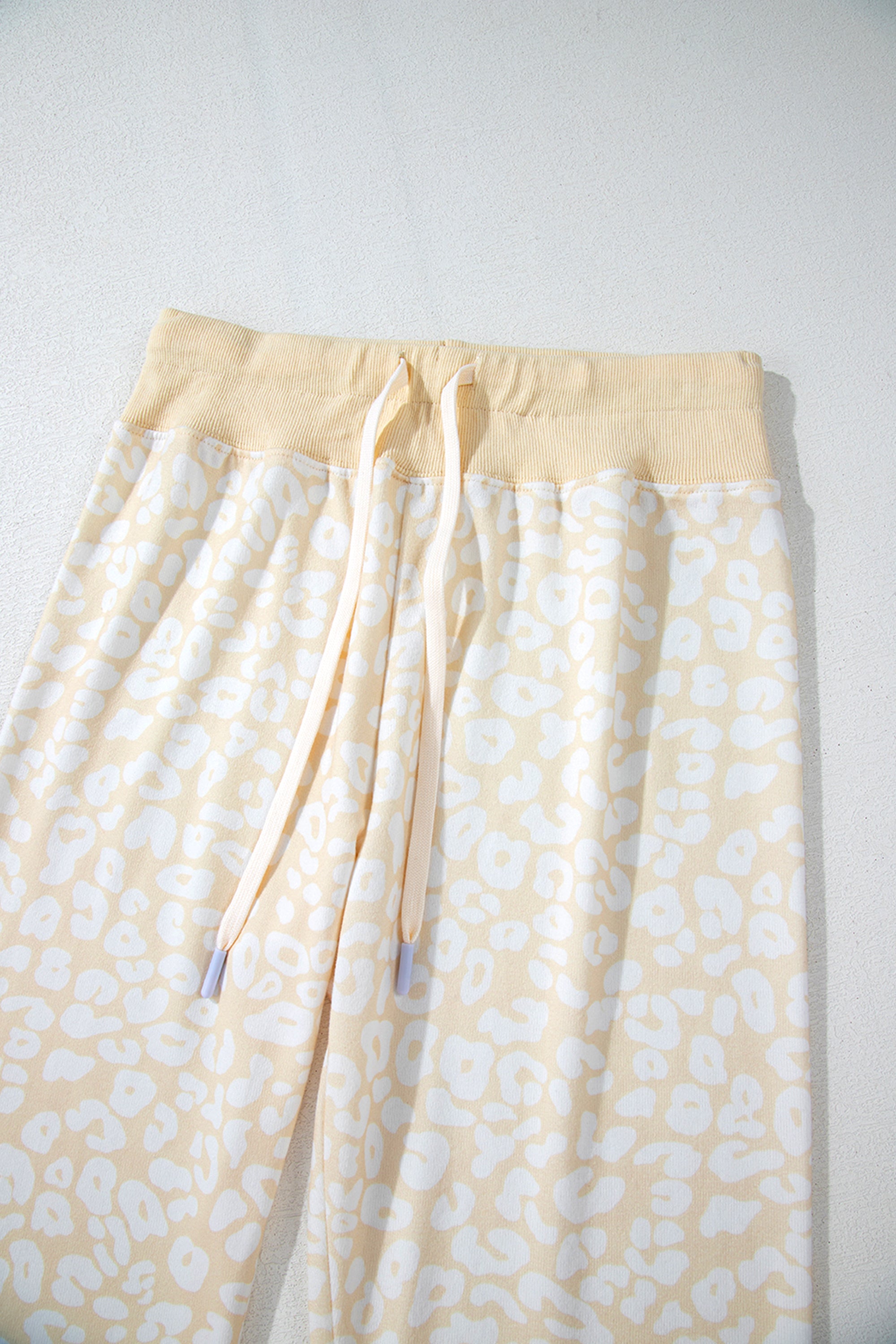 طقم نسائي قطعتين، مكون من بلوزة وبنطلون، لونه أبيض بنقشة الفهد باللون الذهبي المطفي. مصمم لراحتك بقصة فضفاضة وحزام خصر قابل للتعديل، ويتميز بتموجات جميلة على طرف البلوزة.