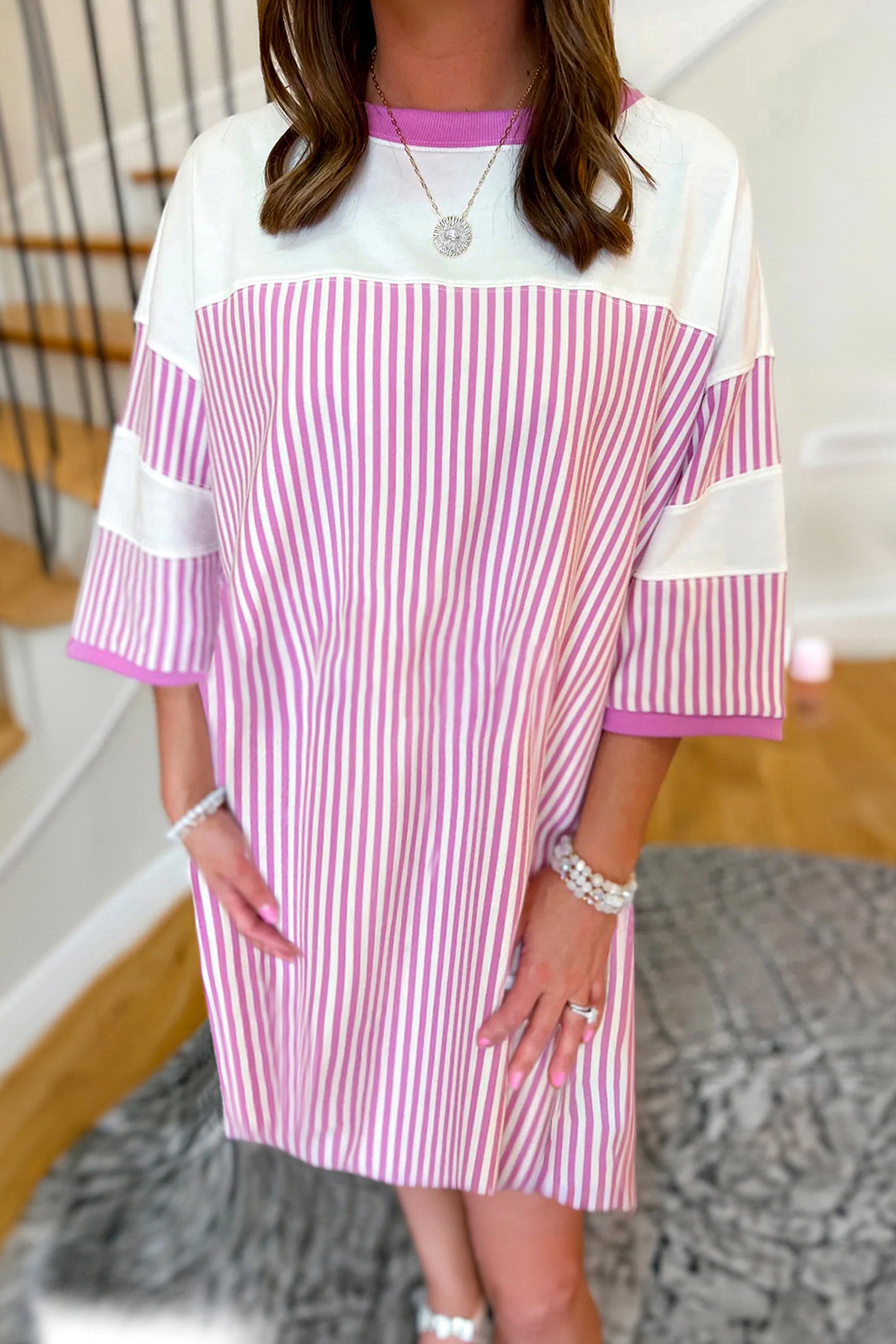 فستان تصميم واسع وجذاب يتميز بقماش مخطط باللونين الوردي والأبيض، ومصمم لإظهار تناسق الجسم. أكمام متوسطة الطول وياقة دائرية كلاسيكية.