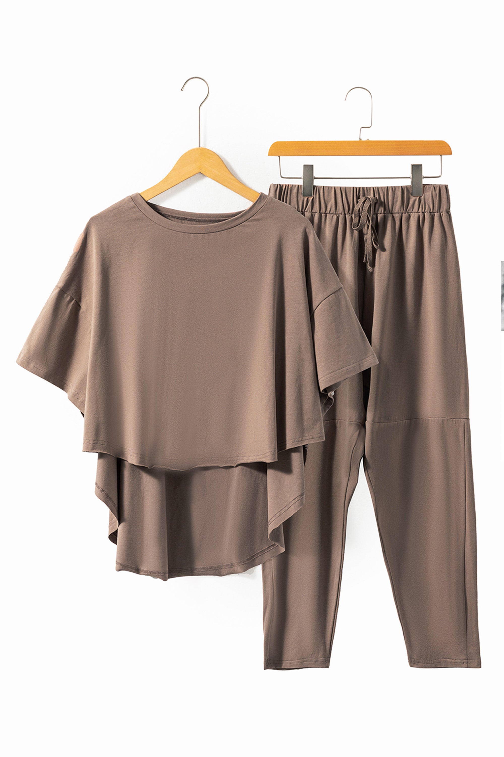 طقم نسائي مكون من بلوزة واسعة بأكتاف منسدلة قصيرة من الأمام وطويلة من الخلف، مع بنطلون بخصر قابل للتعديل وقصة مريحة وقصيرة. مصنوع من قماش ناعم ومرن، ومثالي للاسترخاء أو لزياراتك الغير رسمية. لون بني رمادي.